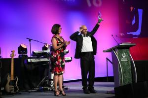 The Anthem Film Festival will return July 8-11, 2026, as a featured event within FreedomFest at Caesars Forum Conference Center, 3911 S A man and a woman on stage with a man making a military style salute with one hand and a statue raised up in the other hand, as the woman stares at him. On stage for Anthem Film Festival. Pretty pink and purple lights are on a screen behind them. The man is in a tuxedo.