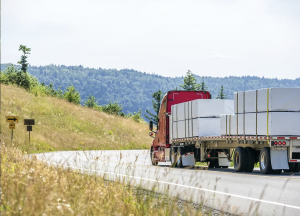 Semi-truck transporting large industrial cargo secured with white industrial shrink wrap on a flatbed trailer.