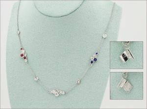 A platinum necklace displayed on a teal velvet bust, featuring a delicate chain set with clusters of round diamonds alternating with small red rubies and blue sapphires at intervals along its length. Two inset photos at right show a close-up of a miniatur