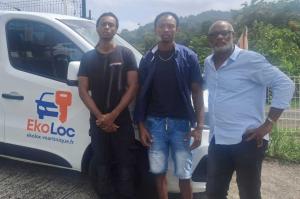 Trois membres de l'équipe EkoLoc Martinique se tiennent devant un véhicule utilitaire blanc floqué du logo de l'entreprise, illustrant le professionnalisme et la proximité du service client proposé par l'agence de location de véhicules basée en Martinique