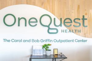 A bright, modern office lobby interior featuring a prominent dimensional sign on a curved white wall that transitions into light wood paneling. The green text reads 