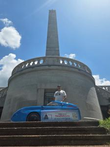 Aaron Novinger stands with his bright blue velomobile at the Abraham Lincoln Memorial in Springfield, Illinois, during his 2,000-mile ride supporting Ponzi scheme victims.