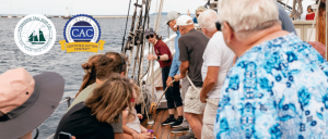Passengers listen to a crew member during a guided sailing experience aboard a Traverse Tall Ship on the water, with the Certified Autism Center™ designation logo displayed.