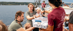 Families and crew members interact aboard a tall ship during a hands-on sailing experience on the water.