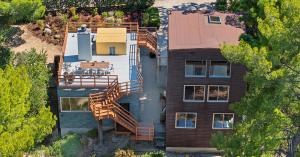 Aerial view of The Benson House, a modern two-story home designed by Frank Gehry with a rooftop deck featuring outdoor seating surrounded by trees and greenery under a clear blue sky in Calabasas Highlands.