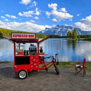 Red Coffee Bike espresso bar beside a lake in Banff National Park, Alberta, during the "THE CROSSING – Canada and USA" documentary journey across North America.