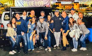 Friends gathered at a nighttime Blue Lot tailgate in Morgantown in front of a Blue Lot Bourbon banner.