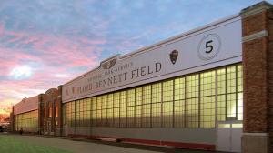Exterior view of the historic Hangar 5 at Floyd Bennett Field in Brooklyn, New York, during sunset. The restored hangar features large industrial glass windows, brick architecture, and prominent 