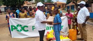 A Pocfarmer representative hands donated supplies to a child while community members gather behind a Pocfarmer banner during a charity event in Africa.