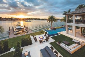 Luxury Naples waterfront home at sunset with a pool, outdoor seating area, private dock and boat overlooking the water.