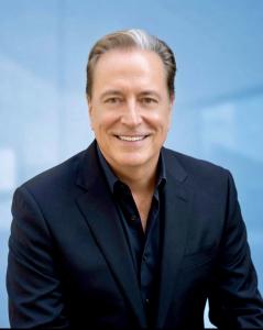 Professional headshot of Robin Green, the newly appointed revenue organization leader and author of The Intelligence Loop, smiling in a dark suit against a blue background.