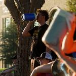 Crowd of individuals are sitting down surround a man drinking from a blue water jug.
