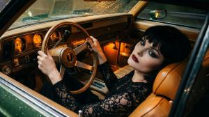 Beyond Disdain singer Selene Calder in a black lace dress seated at the wheel of a vintage car on a rainy night, looking toward the camera with dark makeup and red lips