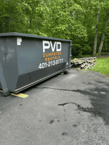 PVD Dumpster Rentals 20-yard roll-off dumpster at a Cranston RI home with demolition debris and wood scraps nearby