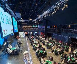 E-sports arena venue with over 25 automatic mahjong tables and participants. One table is on stage for streaming