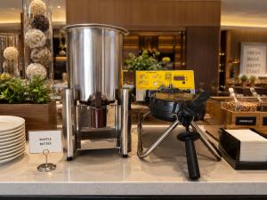 Stainless-steel Golden Waffle batter dispenser beside a commercial rotating waffle maker at a luxury hotel breakfast buffet station.