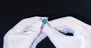 Amorae engagement ring by VERGEZ™, white gold with blue topaz gemstones, held between white-gloved hands.