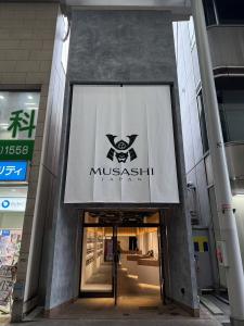 Exterior view of MUSASHI JAPAN Hiroshima Hondori Store with storefront entrance and white MUSASHI JAPAN noren curtain