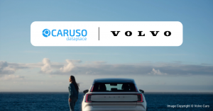 Visuel clé co-brandé montrant les logos CARUSO Dataplace et Volvo au-dessus d'un SUV électrique Volvo blanc au bord de la mer, avec une femme à côté.