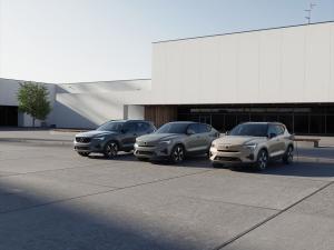 Trois SUV de la série 40 de Volvo, en gris, vert et beige, garés devant un showroom moderne, l'un branché à une borne de recharge.
