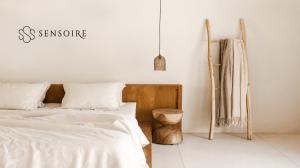 White linen bedding in a minimalist bedroom with a wooden headboard, pendant light and ladder with neutral throws.