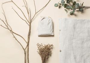 Flat lay of Sensoire natural linen textiles with dried branches and eucalyptus on a neutral background.