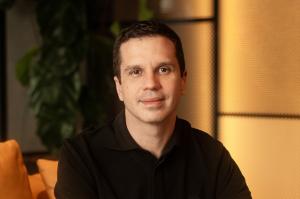 Portrait of Luciano Brandão, CEO and co-founder of VOLL, wearing a black polo shirt and looking at the camera while seated in a modern office with warm lighting and blurred background.