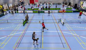 Wide overhead view of multiple pickleball courts on a blue indoor floor at the First Ukrainian Veterans Pickleball Championship in Kyiv, 2026, with dozens of players competing and Ukrainian Pickleball Federation branding on the surrounding walls.