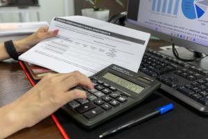 A financial professional using a calculator and reviewing data reports, representing the cross-border asset verification and auditing process for the Hong Kong New CIES net worth assessment.