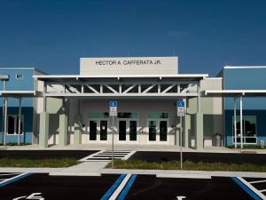 Front entrance of Hector A. Cafferata Jr. K-8 School, featuring a covered walkway, glass doors, and the school's name on the building facade under a clear blue sky.