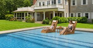 AquaCurve brown in-pool loungers with a matching side table on a shallow sun shelf, with a mother and child relaxing in a backyard pool.