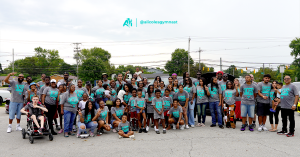 A large group of staff, volunteers and families stands together outdoors at the end of a back-to-school giveaway event.