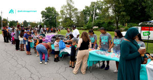 Families line up along outdoor tables stocked with supplies at a community back-to-school giveaway.