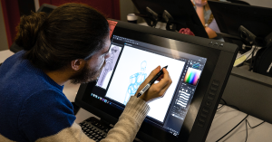 A student uses a stylus on a digital drawing tablet to sketch a character in animation software at a Vancouver Film School classroom workstation.
