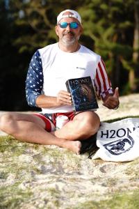 Author Ray Culver holding his debut novel H2ONU, a full-color hardcover, on Kailua beach.