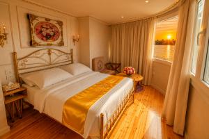 Elegant luxury king cabin aboard Kenzy Dahabeya featuring a gold-accented bed, handcrafted décor, wooden flooring, and large panoramic windows overlooking a spectacular sunset on the Nile River.