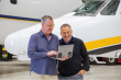 Two men holding a laptop looking at Bluetail aircraft records management software in front of a plane.