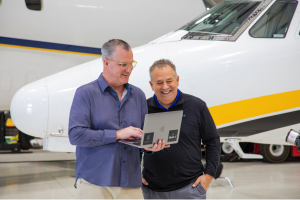 Two men holding a laptop looking at Bluetail aircraft records management software in front of a plane.