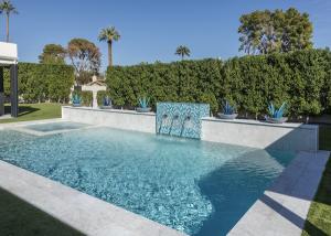 Rectangular pool with a tiled water feature, stone coping and potted blue agave plants against a trimmed hedge at a Phoenix Arizona property
