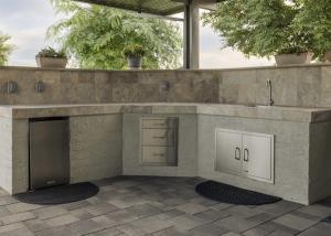 Stone outdoor kitchen with a built-in refrigerator, storage drawers and sink under a pergola on a paver patio at a Phoenix Arizona home