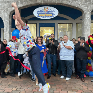 Crowd applauding outside Vincent’s Clubhouse Enrichment Center during a ribbon-cutting event with a person jumping in front.