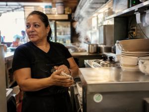 Local restaurant owner working inside a neighborhood business participating in the Secret World creator ecosystem.