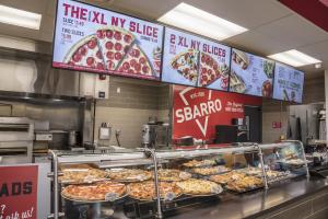 Photo of several XL pizzas behind glass at a Sbarro restaurant for guests to choose from.