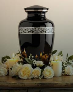 Tranquility Cremation provides direct cremation, direct burial, and pre-planning services to families across Southern Ontario Black memorial urn with silver detailing surrounded by white roses and candles.