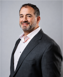 James Prendamano, business leader and educator, pictured in a dark suit and white shirt against a gray background.