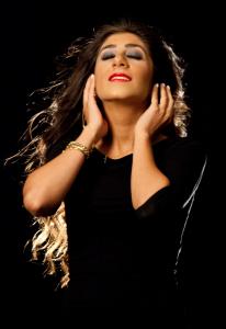 Studio portrait of American coloratura soprano Farrah Mechael wearing black against a dark background with eyes closed.
