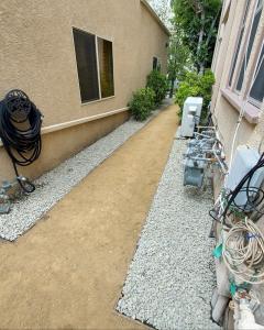 An overhead view of a narrow commercial exterior walkway paved with decomposed granite and lined with grey gravel rocks for stormwater management.