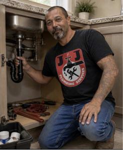 Natalio Pergis, owner of J&J Plumbing Services, kneeling under a residential kitchen sink while inspecting and repairing interior drainage and supply pipes in Bakersfield.