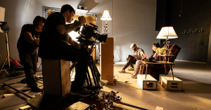 Film crew operating a professional camera while actors perform a scene on set