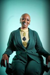 Professional portrait of Steffanie Rivers seated in a dark green suit against a teal studio background.